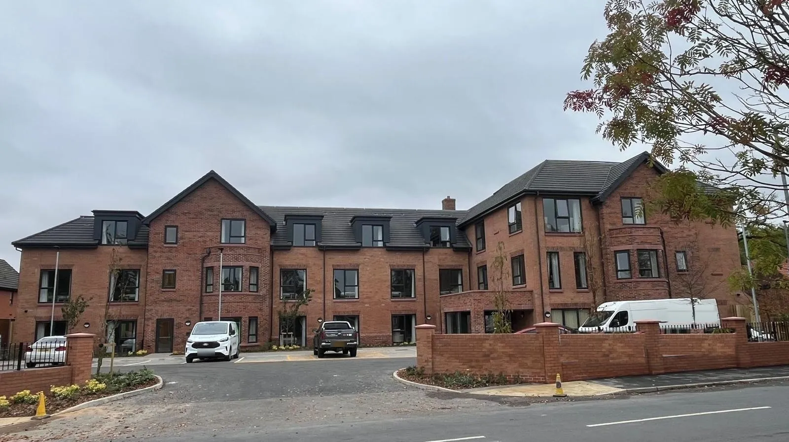 Newly built three-storey red brick care home in Manchester with dormer windows, landscaped car park and a brick boundary wall